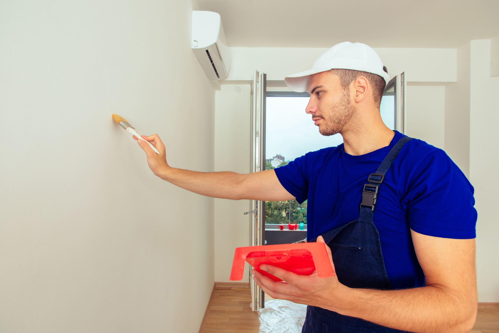 Young painter is coloring his living room in the white color